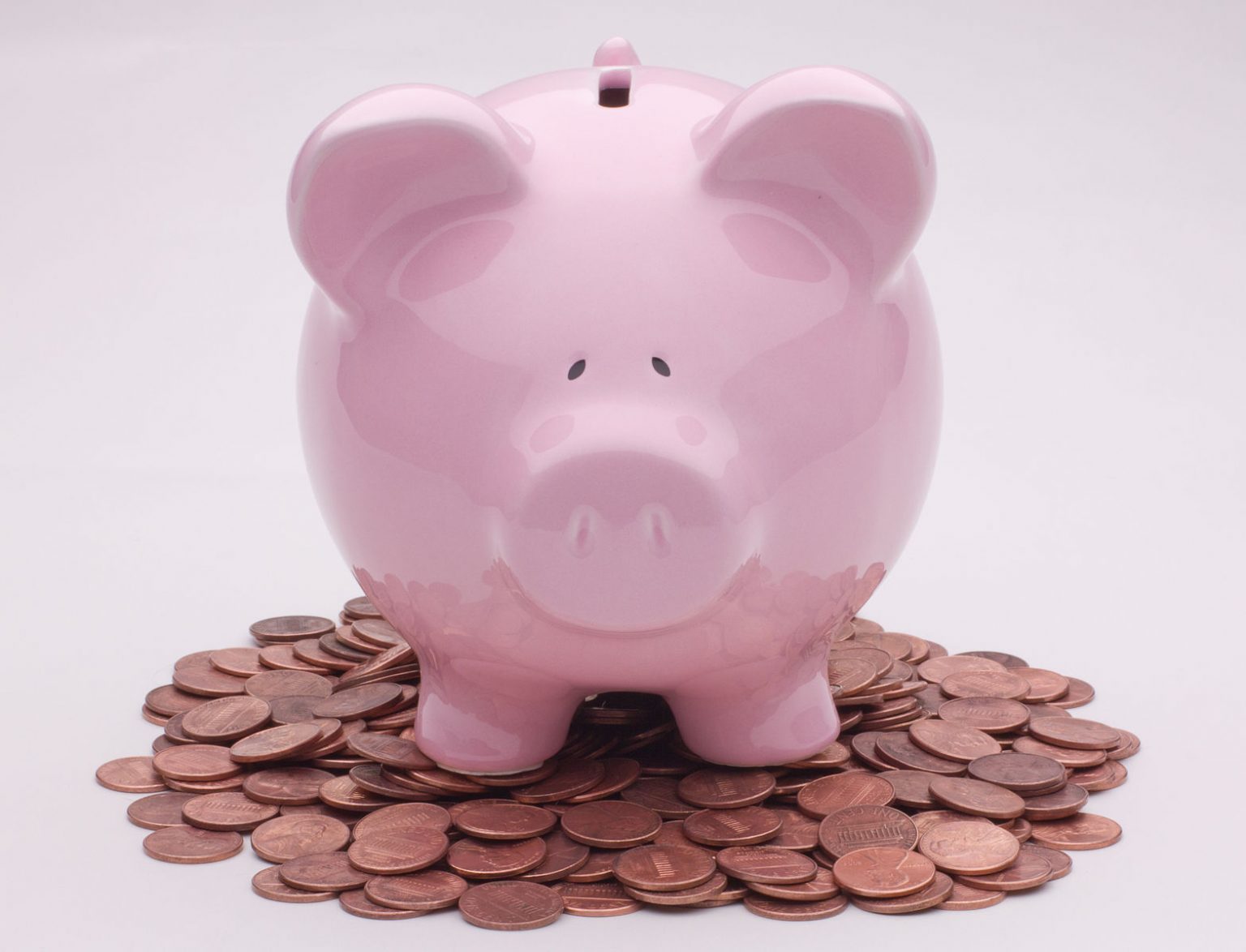 pink ceramic piggybank with smiling face on a white background and standing in a pile of copper pennies