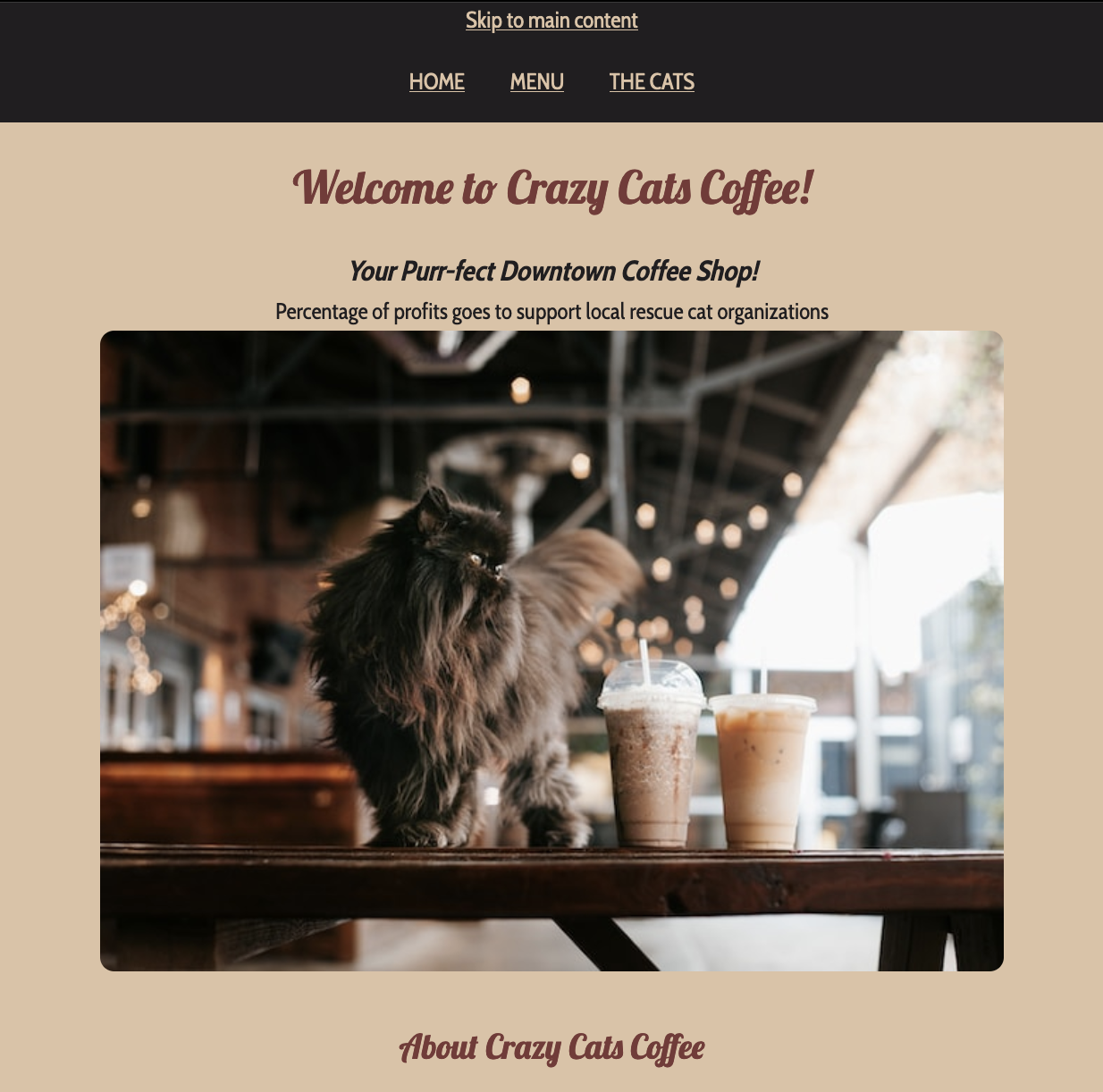 screenshot of Crazy Cats Coffee website. Colour theme is beige and brown. Top navigation is dark black-brown with beige text. It says Skip to main content. underneath there's links to HOME MENU and THE CATS. Below in red-brown calligraphy text is Welcome to Crazy Cats Coffee! The next line says in bold italic black text Your Purr-fect Downtown Coffee Shop! underneath in regular weight and styled black text is Percentage of profits goes to support local rescue cat organizations. There's a picture of a dark brown long haired cat at coffee shop on a dark wood table by two iced coffees in plastic cups. Finally below the photo, in smaller red-brown calligraphy text than the welcome message is About Crazy Cats Coffee
