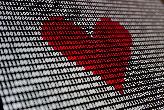 the entire photo is a close up of a screen covered in white binary code - ones and zeros in white text. In the centre of the screen the numbers are red making a red heart.