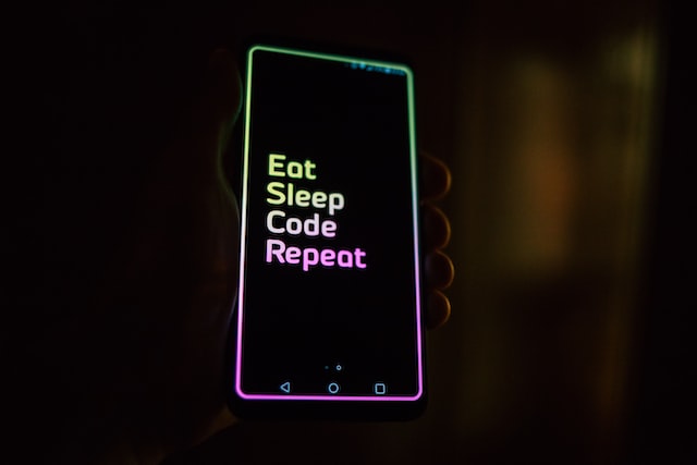 Cell phone with dark screen and neon words saying eat, sleep, code, repeat