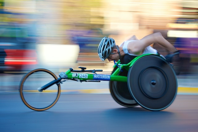 man wearing bicycle helmet in a bright green, 3 wheeled racing wheelchair going fast. The background of the photo is blurred. Stickers on the wheelchair say 248 and Masterson. Photo taken during the 2017 Chicago Marathon