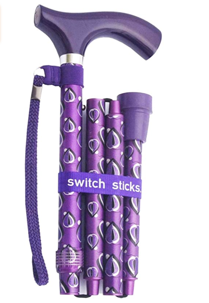 purple metal cane folded up into four sections. It has a darker purple slightly curved t-shaped handle, the same colour rubber tip, and rope wrist strap. The folded cane is wrapped with a purple ribbon or fabric that says Switch Sticks in white letters